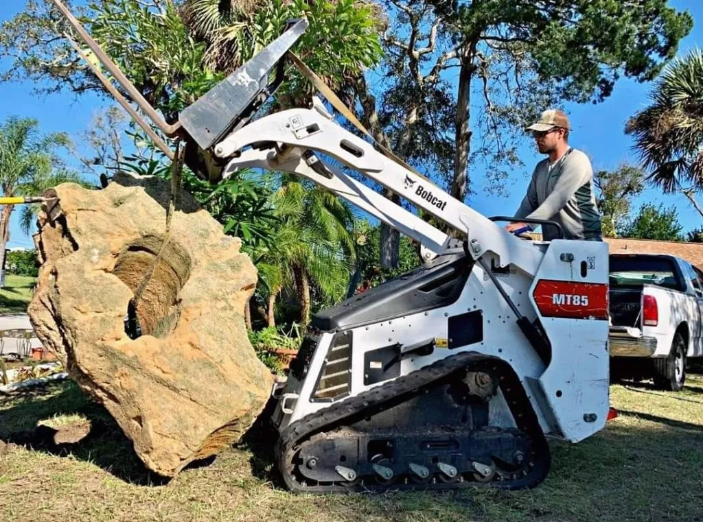Landscapes by Mic using compact equipment to move a large landscape rock