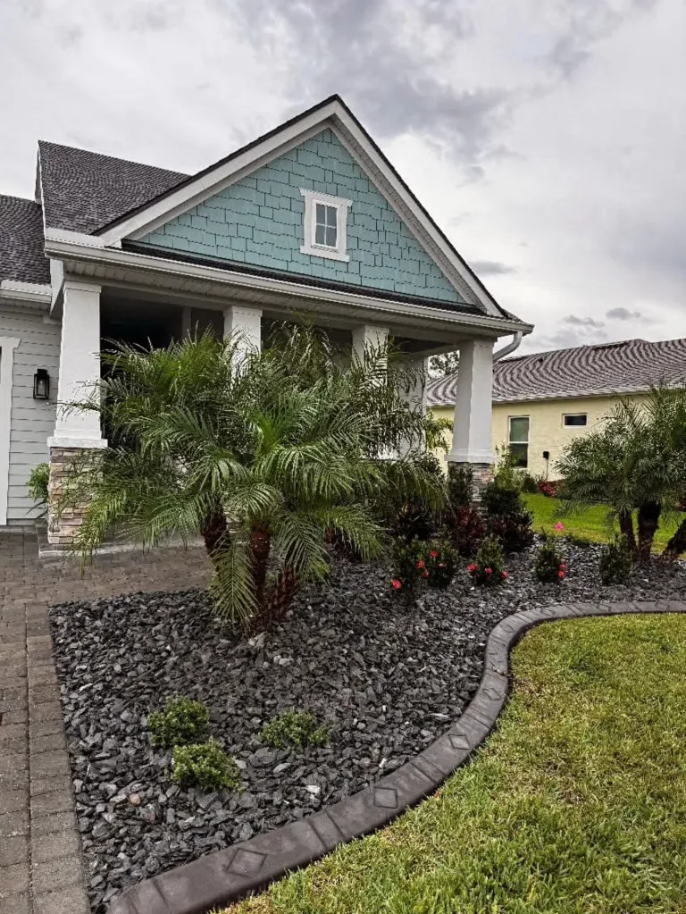 Front landscape with dark decorative rock, palms, and curbing