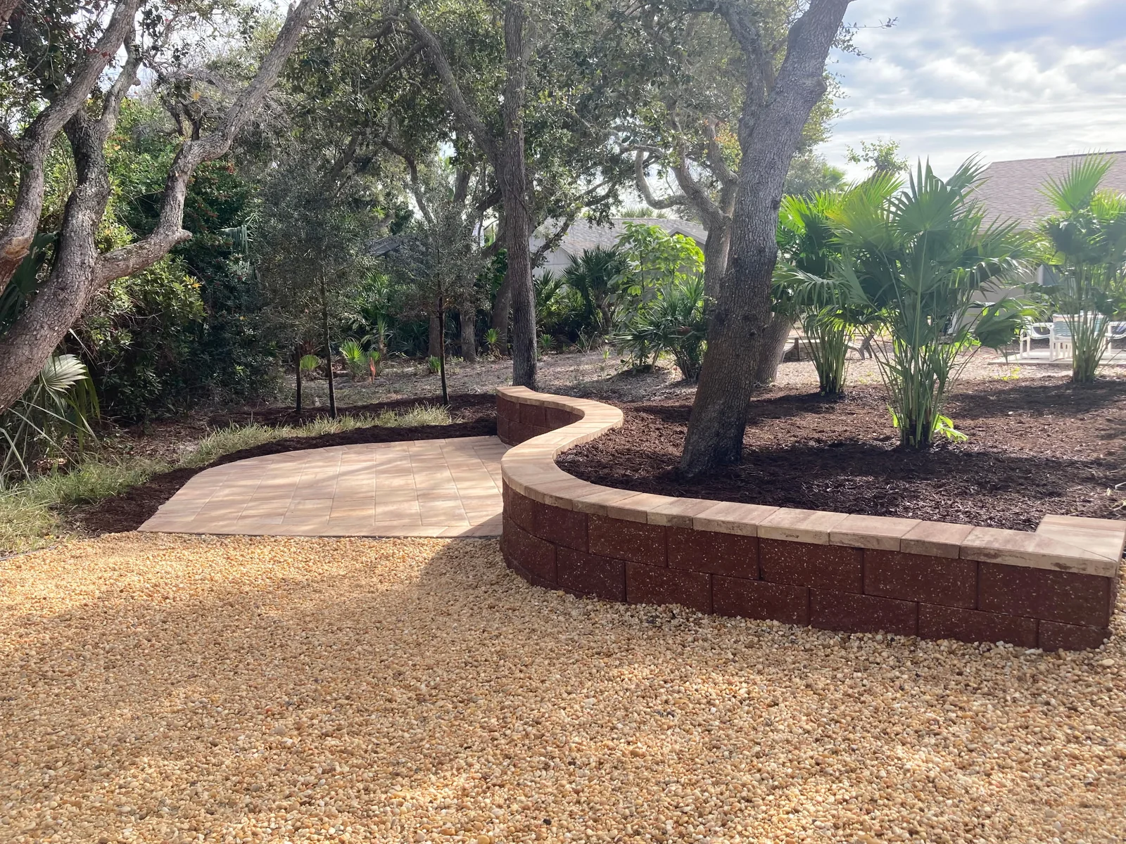 Completed backyard with paver area, curved retaining wall, gravel, mulch and palms