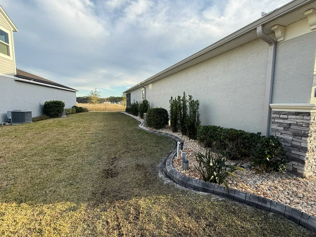 Long side-yard rock bed with screening plants and paver edging